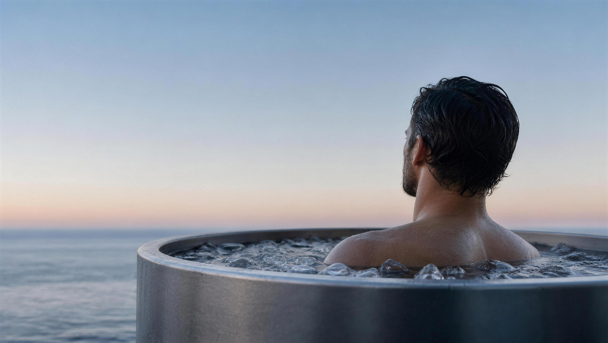 A man in a steel plunge tub at dusk, looking out to the horizon