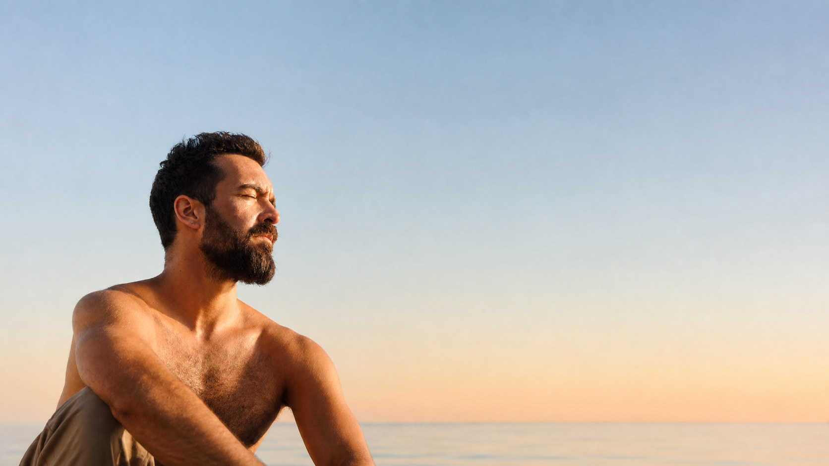 A man sitting in the first sun of the day, sea behind him