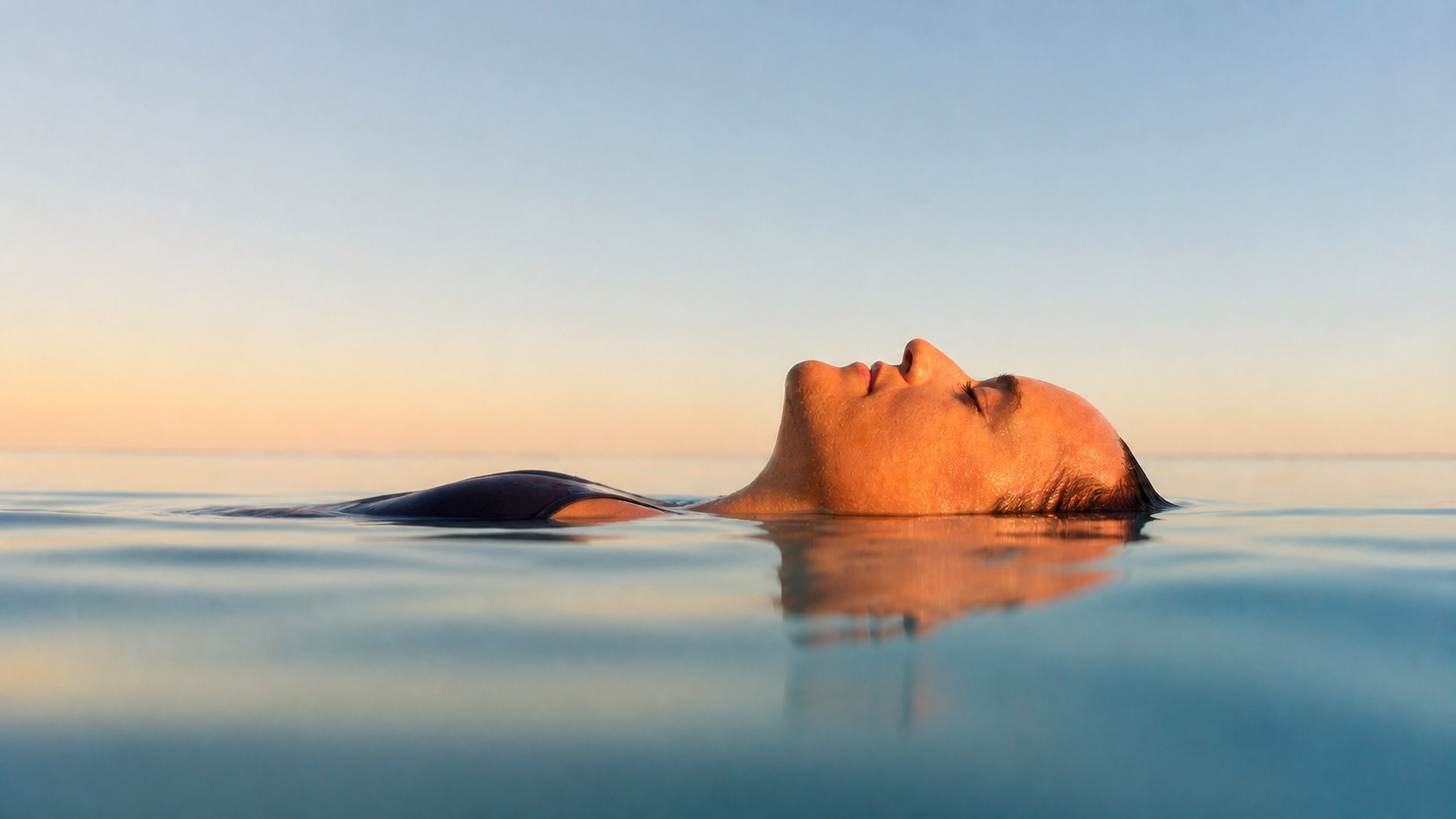 A woman floating on her back in calm water at first light