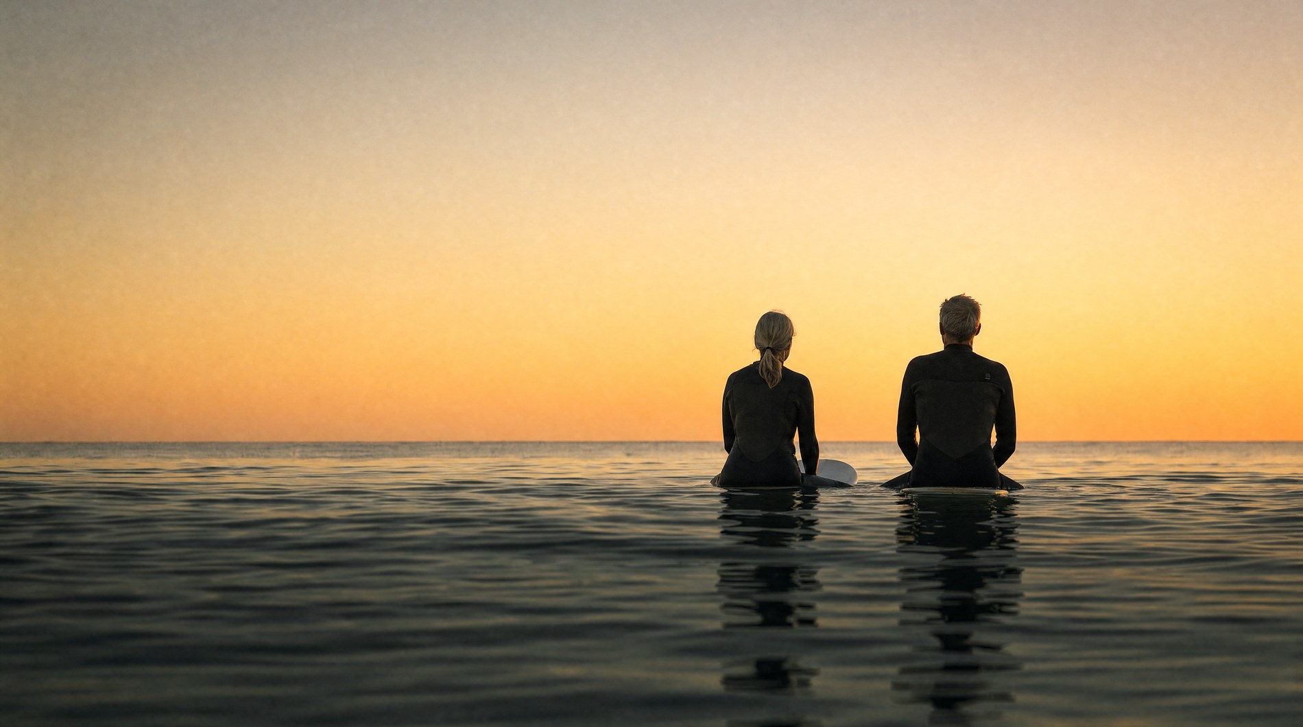 Two surfers sitting on their boards at first light, facing the horizon